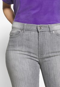 Grå denimjeans med en slät yta, framfickor och silverfärgade detaljer. Matchas med en lila topp.