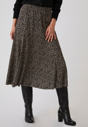 Donna che indossa una gonna midi nera e beige a fantasia, stivali neri al ginocchio con tacco e un top nero a maniche lunghe.