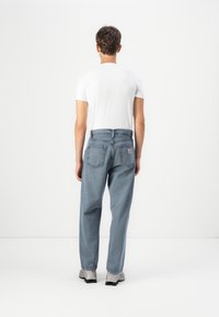 Lyseblå denimjeans med høy midje, løs passform, og to baklommer. Kombinert med en hvit t-skjorte med korte ermer.