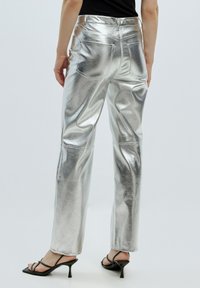 Zilverkleurige metallic wijde broek met een strakke, gladde textuur en opvallende achterzakken. G拖与 zwart met strappy hakken.