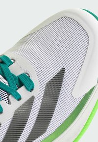White athletic shoe with mesh upper, teal laces, silver accents, and green sole trim. Textured surface includes stripes for design.