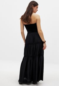 Langes, schwarzes Maxikleid mit einem eng anliegenden, trägerlosen Oberteil und einem gestuften, strukturierten Rock; aus leichtem, fließendem Stoff gefertigt.
