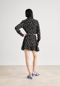 Černé květinové šaty s dlouhými rukávy, volánkovým lemem a vázáním v pase. V kombinaci s modrými sandály na blokovém podpatku. Hladká textura a lehký materiál.