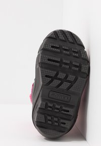 Suela de zapato de goma negra con surcos profundos para tracción. Presenta un logotipo de marca prominente y una superficie texturizada con patrones variados.