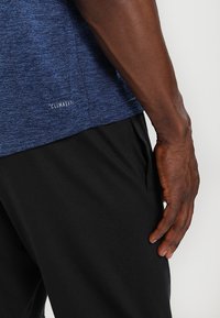 Blåmelerad träningströja tillverkad av andningsbart tyg, med platta sömmar, rund hals och "CLIMALITE"-logga nära fållen.