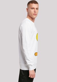 Hvit crewneck sweatshirt med et stort gult tegneseriefigurtrykk på forsiden. Materialet ser mykt ut med ribbestrikkede mansjetter og kant.