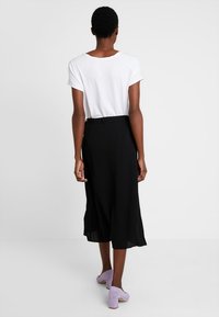 Svart midikjol med en flödande silhuett, ihopparad med en lös vit topp. Kompletterad med lavendelfärgade klackskor med blockhälar.