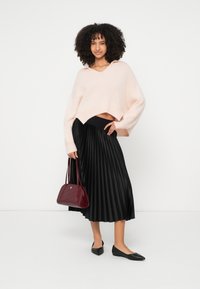 Απαλό ροζ κοντό πουλόβερ, μαύρη πλισέ μίντι φούστα, μαύρες μπαλαρίνες και μπορντό τσάντα χειρός με γεωμετρικές λεπτομέρειες. Λείες υφές και μοντέρνος σχεδιασμός.