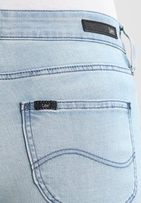 Ljusblå denimjeans har en svart "Lee"-tagg på bakfickan, med en klassisk femficksdesign och subtila sömnadsdetaljer.
