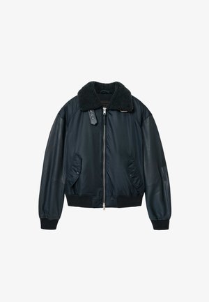 Marineblauwe bomberjack met leren mouwen, een nepbontkraag en elastische manchetten. Voorzien van een ritssluiting en twee steekzakken aan de zijkanten.