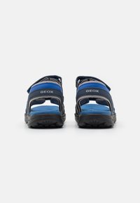 Blå och svarta Geox-sandaler med öppen design, justerbara remmar och texturerade sulor, utformade för andningsförmåga och komfort.