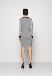 Silberne Strickkleid mit langen Ärmeln, das schwarze Akzente am Ausschnitt und an den Manschetten aufweist. Das Kleid hat eine figurbetonte Silhouette und eine knieumspielende Länge.