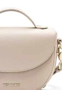 Crème leren schoudertas met een afgeronde klep en bovenhandvat, voorzien van gouden hardware en "HEY MARLY" branding aan de voorkant.