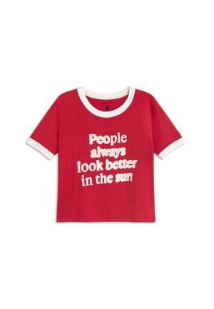 Rotes T-Shirt mit kurzen Ärmeln, weißem Kragen und weißen Ärmelsäumen, mit weißem Text: „Menschen sehen in der Sonne immer besser aus.“