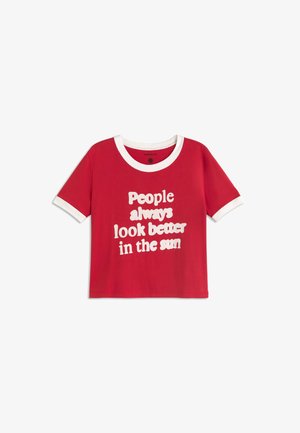 Rotes T-Shirt mit kurzen Ärmeln, weißem Kragen und weißen Ärmelsäumen, mit weißem Text: „Menschen sehen in der Sonne immer besser aus.“