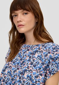 Bloemmotief top met korte mouwen. Heeft een blauw, roze en witte kleurenschema op een donkere achtergrond. Lichtgewicht stof, ontspannen pasvorm.