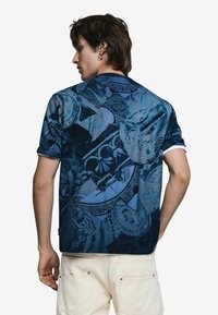 Košeľa s krátkym rukávom v tmavomodrej farbe s prepracovanými vzormi, zahŕňajúca rôzne textúry a odtiene, s kontrastnými bielymi akcentmi na golieri.