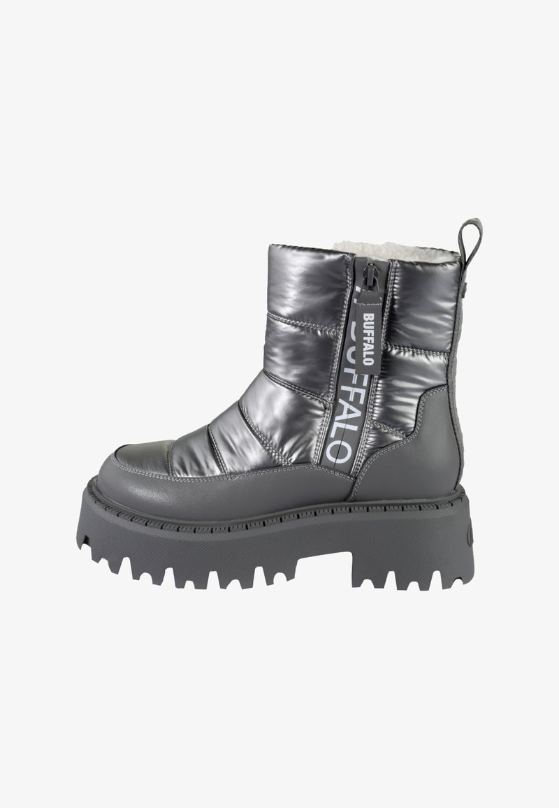 Šedá polstrovaná kotníková bota s lesklým povrchem. Má masivní podrážku, kontrastní černý akcent na patě, boční zip a logo.