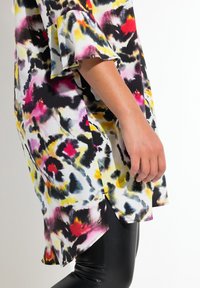 Bunte Bluse mit einem auffälligen, abstrakten Tierdruck in Gelb, Pink, Schwarz und Weiß. Ausgestellte Ärmel und seitliche Schlitze verleihen dem Design eine besondere Note.