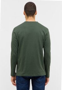 Långärmad t-shirt med rund halsringning i mörkgrön bomull, med en mjuk yta och avslappnad passform, bärs med blå jeans.