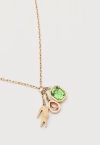 Chaîne en or avec trois pendentifs : une pierre précieuse octogonale verte, une pierre précieuse rose en forme de goutte, et une forme de crocodile texturée en or.