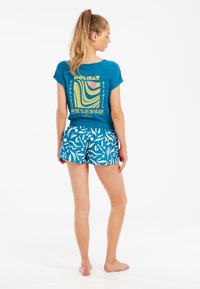 Blå t-shirt med grafiskt tryck och korta ärmar, ihopparad med blå shorts som har ett vitt bladmönster. Tillverkat av bomull, avslappnad passform.