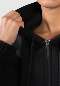 Black zip-up hoodie made of soft cotton, featuring a drawstring hood, ribbed cuffs, and a metallic zipper with a smooth finish.