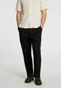 Jasny beżowy podkoszulek z krótkimi rękawami, wykonany z otwartej dzianiny, w połączeniu z czarnymi zwężającymi się spodniami i brązowymi butami w stylu mokasynów.