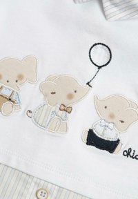 Camisa blanca con elefantes bordados en beige y marrón claro, vistiendo trajes con estampados. Los detalles destacados incluyen un globo negro y acentos azules.