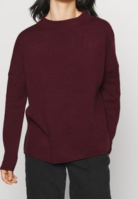 Maglione bordeaux realizzato in morbido tessuto a maglia, con un collo alto e una vestibilità comoda, spalle scese e polsini a coste.
