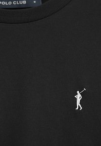 Svart tyg med vit Polo Club-märkeslogotyp som visar en liten broderad figur av en person som bär en polomallette på bröstet.