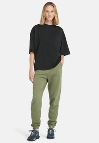Černé oversized tričko, zelené jogger kalhoty s elastickými lemy a černé turistické boty s texturovaným detailem. Minimalistický design a volný střih.
