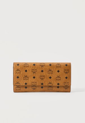 Portefeuille en cuir marron avec logos MCM noirs, emblèmes ailés et motifs en losanges sur fond blanc uni.