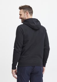 Felpa nera con cappuccio indossata da una persona, caratterizzata da una texture morbida e un orlo a costine, con una vestibilità rilassata e una tasca a marsupio sul davanti.