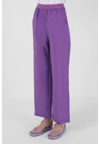 Purple wide-leg pants with an elastic waistband in lightweight fabric. Features a smooth texture and a relaxed fit. Paired with purple sandals.
