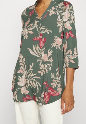 Blusa floral en verde oscuro con estampados de mariposas y plantas en rosa y rojo. Presenta un escote en V y mangas de tres cuartos. Tejido suave.