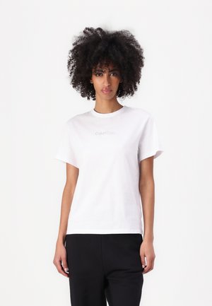 Witte katoenen T-shirt met een ronde hals, korte mouwen en een subtiele Calvin Klein-logo gedrukt op de voorkant, gecombineerd met zwarte broek.