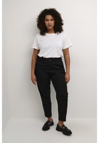 Černé elegantní kalhoty se slim fit, zkombinované s jednoduchým bílým tričkem a černými mokasíny. Hladký povrch, standardní zapínání na knoflík.