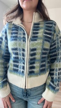 Pull en tricot zippé avec un col de couleur crème. Présente un motif géométrique bleu et vert ; ourlet et poignets côtelés ; texture douce.