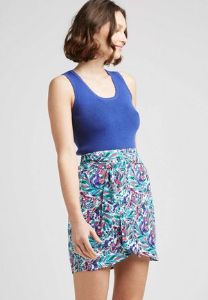 Un débardeur bleu côtelé associé à une jupe florale colorée arborant des motifs verts, roses et violets, nouée à la taille.