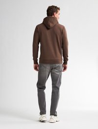 Felpa a collo alto marrone con cappuccio regolabile, abbinata a jeans grigi. La felpa presenta una texture semplice e liscia; i jeans hanno tasche posteriori.