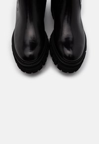 Stivaletti neri in pelle con finitura lucida, suola in gomma robusta, punta arrotondata e dettagli di cucitura sottili.