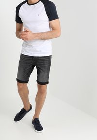 Biała i granatowa koszulka typu raglan w zestawieniu z ciemnoszarymi szortami dżinsowymi. Strój dopełniają granatowe trampki i prosty design.