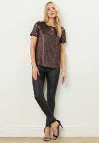 Bronze pailletteret top med korte ærmer, parret med sorte tætsiddende bukser og sorte høje hæle. Outfittet har en subtil glans og et elegant design.