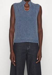 Jersey de punto sin mangas en azul oscuro con un patrón texturizado y un cuello alto. El dobladillo presenta un detalle de canalé, complementado por un corte holgado.