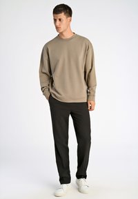 Felpa beige con scollatura rotonda e spalle scese, abbinata a pantaloni neri a gamba dritta e sneakers bianche.
