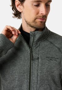 Giacca grigia con zip, in tessuto texturizzato, colletto alto e zip verde. Presenta un logo sul petto. Motivo sottile su tutta la superficie.