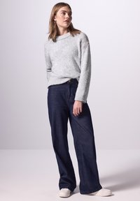 Hellgrauer, flauschiger Pullover kombiniert mit dunkelblauen, weit geschnittenen Jeans und weißen Sneakern. Das Outfit zeichnet sich durch eine lockere Passform und minimale Verzierungen aus.