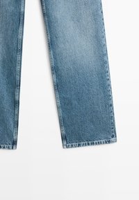 Blue denim jeans legs with visible stitching on a white background, showing a straight cut and faded texture.