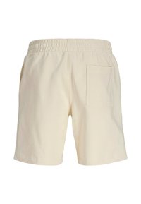 Short beige en coton avec une ceinture élastique, doté d'une poche arrière unique et d'un tissu lisse légèrement texturé.